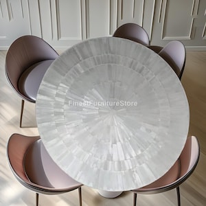 May include: A circular dining table with a white, mosaic surface, encircled by four chairs. The chairs have brown backs and pink seats, with slender, dark metal legs. The table's surface has a radial design. The text "FinestFurnitureStore" is visible.