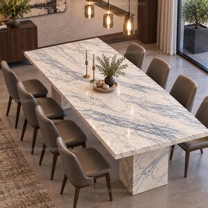 Può includere: Un tavolo da pranzo rettangolare con piano in marmo bianco e blu e base a piedistallo abbinata, circondato da otto sedie imbottite grigie con gambe in legno scuro. Il tavolo è decorato con due candelabri dorati e una piccola pianta.