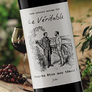 Peut inclure: Une bouteille de vin avec une étiquette illustrant deux hommes en noir et blanc. L'étiquette indique "Le Véritable" et "Veux-tu être mon témoin ?" Un verre de vin rouge et des raisins sont visibles en arrière-plan.