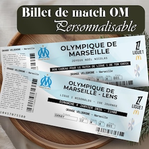 Peut inclure: Deux billets de match de l'Olympique de Marseille bleu clair avec le logo de l'équipe et du texte. Les billets sont pour un match de Ligue 1 au stade Orange Vélodrome. Les billets sont personnalisés et portent la mention "Billet de match OM Personnalisable".
