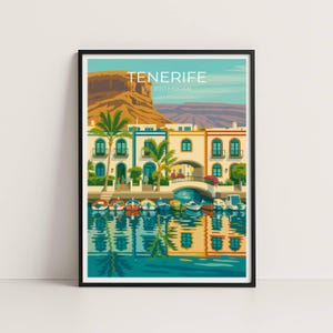 Puede incluir: Una impresión artística enmarcada con una colorida ilustración de Tenerife, Puerto Mogán. La obra representa una escena costera con edificios, barcos, un puente y palmeras. El cielo es azul claro y el agua refleja los edificios y barcos.