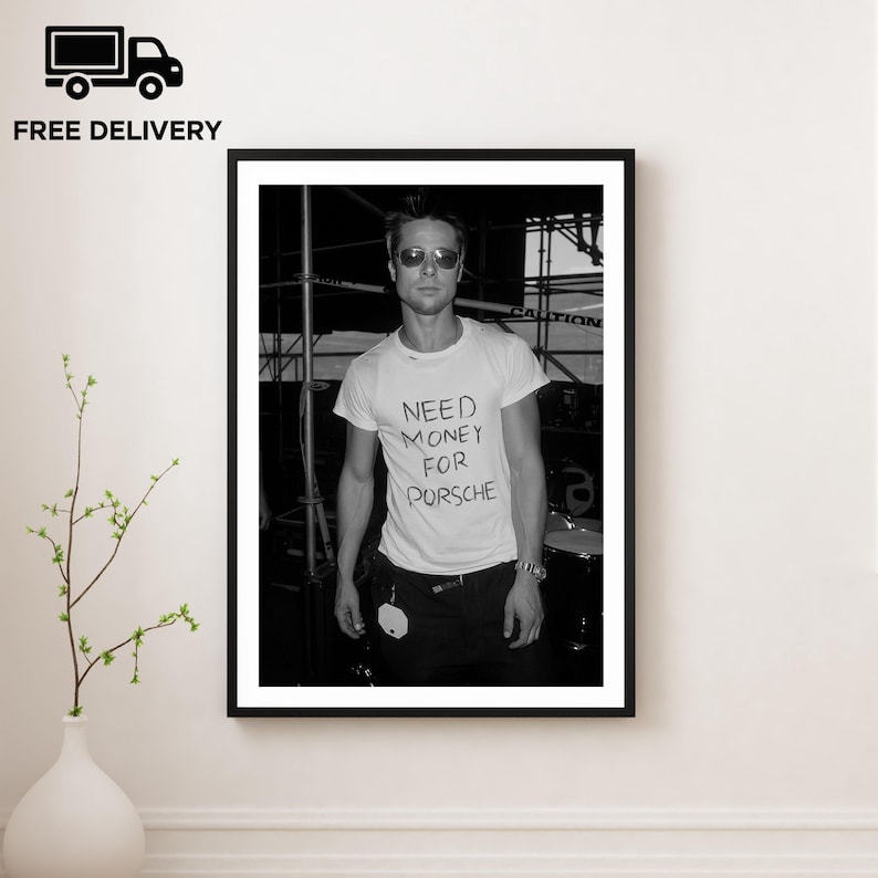 May include: Black and white framed print featuring a person wearing sunglasses and a white t-shirt with the handwritten text "NEED MONEY FOR PORSCHE". The image is a portrait, with a black frame and a white background.