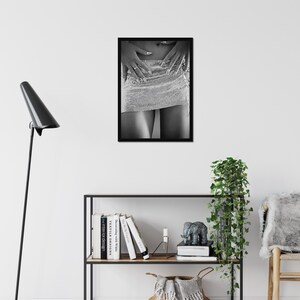 May include: Black and white framed print featuring a close-up of a sparkling, silver mini-skirt. The image shows a person's legs and hands resting on the skirt. The nails are long and painted. The print is displayed on a white wall.