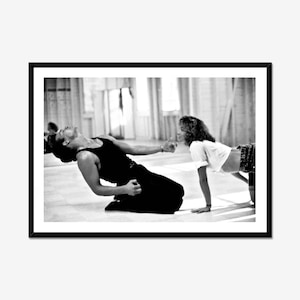 Peut inclure: Photographie encadrée en noir et blanc de deux personnes dans un studio de danse. L'une est à genoux, vêtue d'un débardeur et d'un pantalon noirs, la tête en arrière. L'autre porte un t-shirt blanc et un pantalon à motifs, penchée en avant.