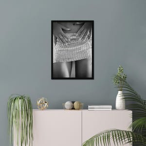 May include: Black and white framed photograph of a silver rhinestone mini skirt. The skirt is the focal point, with hands gently resting on it. The image is a close-up, emphasizing the texture and sparkle of the skirt.
