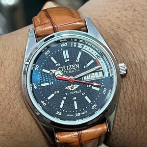 May include: A Citizen automatic wristwatch with a dark blue face, silver bezel, and brown leather strap. The watch face displays the day and date, with a red second hand. The watch is marked "21 Jewels" and "Japan 30 Made."