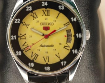 Montre automatique Seiko 5 reconditionnée ; cadran jaune, date 17 rubis, bon état.