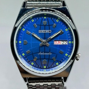 May include: A silver Seiko automatic wristwatch with a blue dial featuring a world map design. The watch has a date display showing "SUN 22" and a silver strap. The watch face also displays the word "SEIKO" and "Automatic".