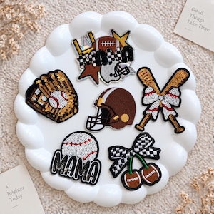 Puede incluir: Un conjunto de seis parches bordados con temática deportiva, que incluye un guante de béisbol con lentejuelas, un casco de fútbol americano, bates de béisbol cruzados con un lazo, una pelota de béisbol con la palabra MAMA y diseños de fútbol.