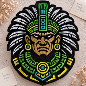 May include: A circular embroidered patch featuring a stylized figure wearing a large feathered headdress. The design uses black, gold, white, lime green, and cyan thread. The figure has a stern expression, circular earrings, and a wide collar.