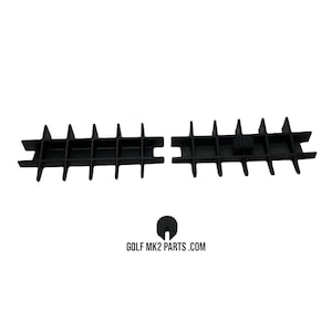 Puede incluir: Piezas de automóvil de plástico negro, que incluyen dos inserciones de rejilla y una pequeña pieza en forma de engranaje. Las piezas tienen un diseño similar a una rejilla y están sobre un fondo blanco. El texto "GOLF MK2 PARTS .COM" es visible.