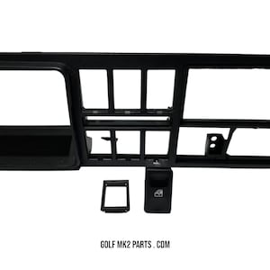 May include: Black dashboard panel with multiple rectangular openings and a window control switch. The panel includes a small rectangular frame and the text "GOLF MK2 PARTS . COM".
