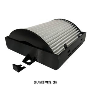 May include: A black air filter assembly with a white pleated filter. The assembly has a rectangular base and a curved top. The text "GOLF MK2 PARTS . COM" is printed at the bottom.