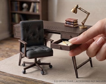 May include: A miniature 1:12 scale office chair with a dark grey tufted seat and backrest, featuring a brown wooden frame and a five-point base with rolling castors. The chair is positioned next to a miniature wooden desk with a drawer.