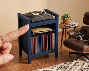 May include: A 1:12 scale miniature dark blue record player and storage cabinet. The top features a black turntable, while the lower shelf holds a row of colourful vinyl records. The text 1:12 SCALE RECORD PLAYER AND STORAGE CABINET is visible.