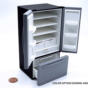 May include: A miniature black refrigerator with open doors revealing white interior shelves, drawers, and door bins. A gray freezer drawer is pulled open at the bottom. A copper penny is placed next to the unit for scale. Text reads: COLOR OPTION SHOWN: ASH GRAY.