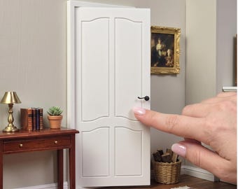 May include: A white 1:12 scale miniature panel door with a matching door frame. The door features four rectangular panels with arched tops and a small black handle. The text at the bottom of the image reads 1:12 SCALE PANEL DOOR & DOOR FRAME.