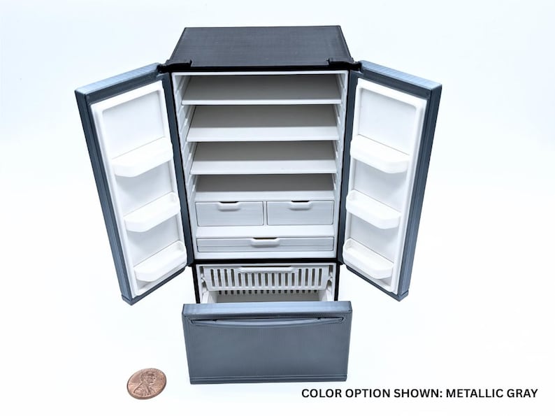 May include: A miniature metallic gray refrigerator with two open doors, multiple white interior shelves, two small drawers, and a bottom freezer drawer pulled open. A copper penny is placed next to the unit for scale. Text reads: COLOR OPTION SHOWN: METALLIC GRAY.