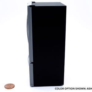 May include: A miniature refrigerator model featuring a solid black side panel and an ash gray front door with a vertical handle. A copper-colored penny is placed on the surface next to the unit for scale. The text COLOR OPTION SHOWN: ASH GRAY is visible.