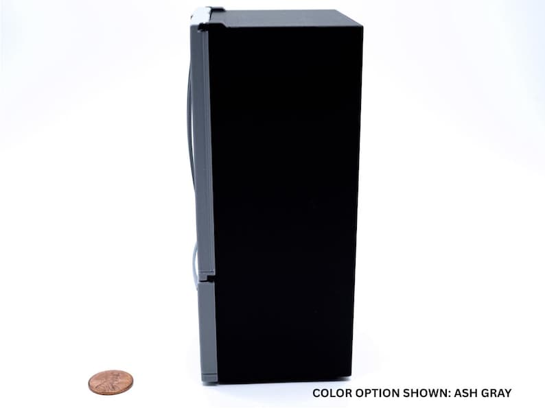 May include: A miniature refrigerator model featuring a solid black side panel and an ash gray front door with a vertical handle. A copper-colored penny is placed on the surface next to the unit for scale. The text COLOR OPTION SHOWN: ASH GRAY is visible.