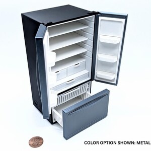 May include: A miniature black and metallic gray refrigerator with open double doors and an open bottom freezer drawer. The interior features white shelves and storage compartments. A copper penny is placed next to the unit for scale. Text reads: COLOR OPTION SHOWN: METALLIC GRAY.