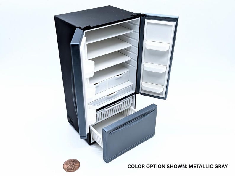 May include: A miniature black and metallic gray refrigerator with open double doors and an open bottom freezer drawer. The interior features white shelves and storage compartments. A copper penny is placed next to the unit for scale. Text reads: COLOR OPTION SHOWN: METALLIC GRAY.