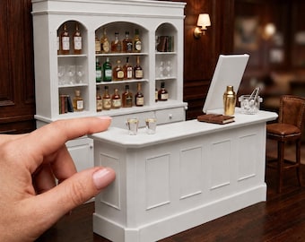 May include: A 1:12 scale white miniature bar counter and cabinet set featuring three arched shelves filled with tiny liquor bottles and glassware. The counter includes a gold shaker, ice bucket, and two small glasses. Text reads: 1:12 SCALE BAR COUNTER AND CABINET SET | ACCESSORIES NOT INCLUDED.