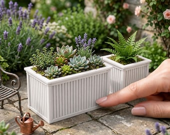 May include: Two white rectangular planter boxes with vertical slat detailing. The larger box contains various miniature succulents and lavender sprigs. The smaller box holds a green fern. Text on the image reads 1:12 SCALE PLANTER BOXES.