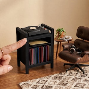 Pu&ograve; includere: Una console giradischi in miniatura nera con un piatto rotante sulla parte superiore, un ripiano centrale con un oggetto piatto e un ripiano inferiore riempito con una fila di dischi in vinile colorati, accanto a una poltrona in miniatura marrone.