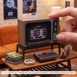Könnte beinhalten: Ein 1:12 maßstabsgetreuer, brauner Miniatur-Röhrenfernseher, der einen Retro-Videospielbildschirm mit einem Punktestand von 00100 anzeigt. Der Fernseher steht auf einem schwarzen Ständer, zusammen mit einer Spielkonsole, einem Joystick und zwei Spieleboxen.