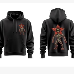 Pode incluir: Moletom preto com um gr&aacute;fico Demogorgon na frente e atr&aacute;s. O design Demogorgon &eacute; vermelho, marrom e bege. O moletom tem capuz e bolso frontal. O gr&aacute;fico &eacute; uma ilustra&ccedil;&atilde;o estilizada da criatura.