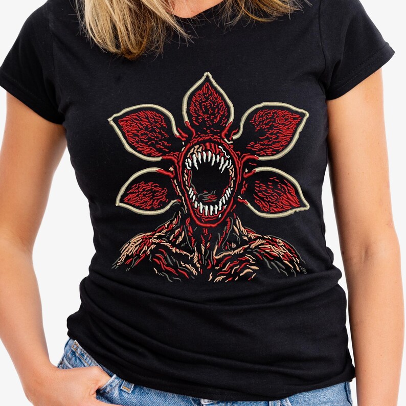 May include: Black t-shirt featuring a red and white graphic of a Demogorgon from the Stranger Things series. The Demogorgon has a flower-like head with sharp teeth and a detailed, textured body. The design is centered on the shirt.