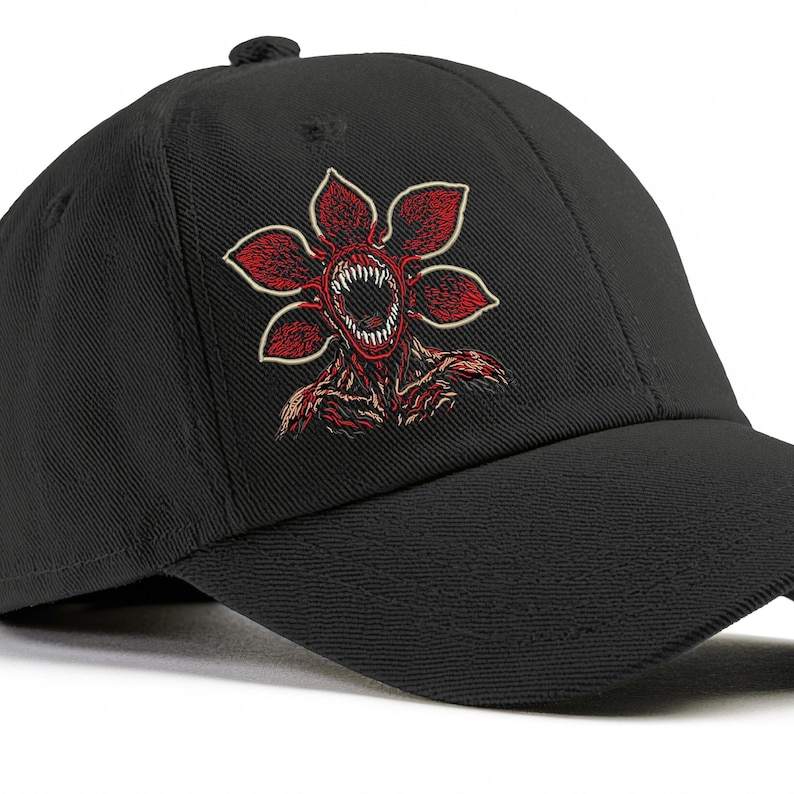 May include: Black baseball cap featuring a red and white Demogorgon flower design. The embroidered graphic depicts a monster with a toothed mouth and petal-like shapes. The cap has a curved brim and a button on top.