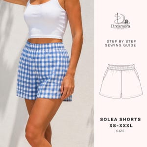 Può includere: Pantaloncini a quadretti vichy blu e bianchi con elastico in vita. L'immagine include un disegno tecnico dei pantaloncini, il testo Dreamora Studio, Step by Step Sewing Guide, Solea Shorts e la gamma di taglie XS-XXXL su sfondo chiaro.