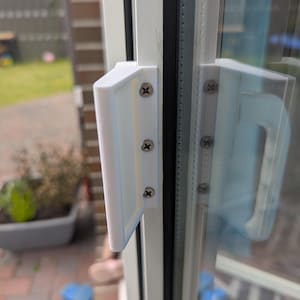 Könnte beinhalten: Nahaufnahme eines weißen Fenstergriffs mit rechteckigem Design, befestigt mit Schrauben. Der Griff ist an einem weißen Fensterrahmen montiert, mit einer Glasscheibe, die die Umgebung reflektiert. Tageslichtaufnahme.