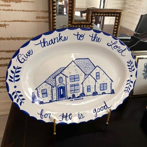 May include: White oval serving platter with a blue scalloped edge and a blue illustration of a house. The platter has the text "Give thanks to the Lord for He is good" in blue script.