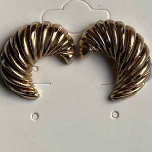 May include: A pair of gold-coloured, half-hoop earrings. Each earring features a textured, ridged design that curves inwards. The earrings are displayed on a white card with a small hole for hanging.