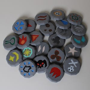 Puede incluir: Un conjunto de fichas grises, circulares, con varios símbolos coloridos. Las fichas presentan diseños en azul, rojo, amarillo, verde y blanco. Los símbolos incluyen llamas, estrellas y formas geométricas. Las fichas están sobre una superficie blanca.