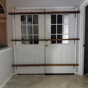 May include: White double doors with glass panes and a dark wooden bar across the top, middle, and bottom. The doors have a gold doorknob and are set in a white frame. The floor is a light beige tile.
