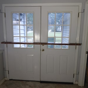 May include: A pair of white French doors with glass panes and a wooden bar across the middle. The doors have a brass doorknob and are framed by a white trim. The bar is held in place by metal brackets.