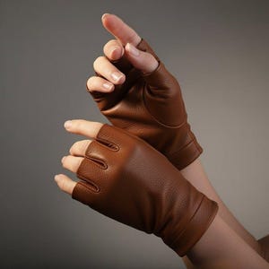 Pode incluir: Luvas sem dedos de couro marrom. As luvas são de uma cor marrom rica e quente e parecem ser feitas de couro macio. O design apresenta aberturas para os dedos e um punho. As luvas são provavelmente para moda ou condução.