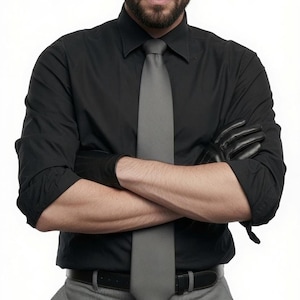 A man with crossed arms wearing a black shirt and grey tie wears black leather gloves.