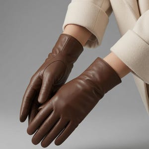 Pode incluir: Um par de luvas de couro castanho escuro liso com um design simples e sem adornos. As luvas apresentam um corte clássico que se estende para além do pulso, exibindo um acabamento limpo e polido com detalhes de costura visíveis nos dedos.
