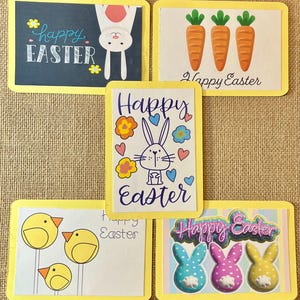May include: A collection of five Easter-themed cards with yellow borders. The cards feature illustrations of carrots, chicks, bunnies, and the text "Happy Easter". One card has a chalkboard design with a bunny and the text "Happy Easter".
