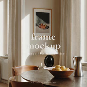 Könnte beinhalten: Esszimmer-Szene mit einem gerahmten Kunstwerk mit Früchten, einer weißen Lampe und einem Holztisch. Der Text "frame mockup" ist überlagert. Eine Holzschale enthält gelbe Früchte, und eine silberne Kanne steht auf dem Tisch.