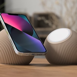 Może przedstawiać: Nowoczesna stacja ładująca do telefonu z beżowym, żebrowanym designem. Smartfon z kolorowym ekranem spoczywa na jednej z kulistych podstaw. Obecna jest również druga, podobna podstawa z białą powierzchnią ładującą.