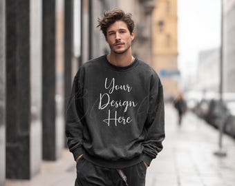 May include: Dark grey sweatshirt with the text "Your Design Here" in white script. The sweatshirt is part of a matching set with dark grey trousers. The person is standing on a pavement.