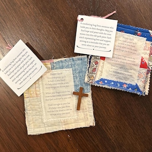 May include: Three small, handmade prayer quilts with attached tags. The quilts are made of patchwork fabric in various colors and patterns. One quilt has a small wooden cross attached. The tags contain inspirational text.