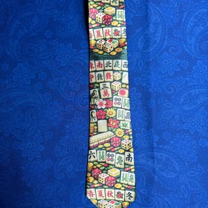 Może przedstawiać: Kolorowy krawat z wzorem kostek do gry, płytek Mahjong i chińskich znak&oacute;w. Krawat ma mieszankę kolor&oacute;w czerwonego, ż&oacute;łtego, zielonego i białego. Tekst na krawacie zawiera chińskie znaki i słowa "Lato", "Jesień" i "Zima".