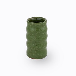 May include: A green ceramic tumbler with a textured, ridged design. The cylindrical cup has a slightly flared opening and a reddish-brown base. The overall aesthetic is rustic and handcrafted.